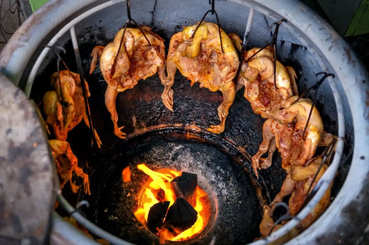 Whole chickens cooking in a traditional tandoor oven over hot charcoal